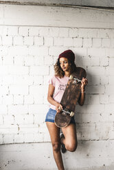 Portrait of a young woman with skateboard, leaning against wall - UUF14253