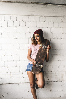 Porträt einer jungen Frau mit Skateboard, an die Wand gelehnt - UUF14253