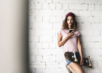 Portrait of a young woman with skateboard, leaning against wall - UUF14254