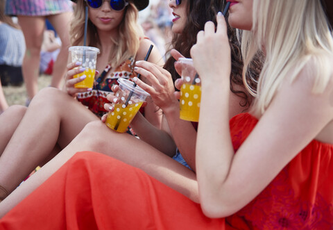 Freunde trinken Saft und sitzen auf einer Wiese während eines Musikfestivals, lizenzfreies Stockfoto