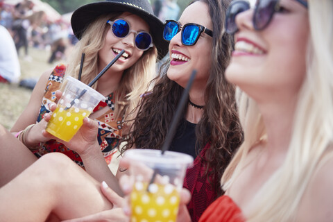 Freunde trinken Saft und sitzen auf einer Wiese während eines Musikfestivals, lizenzfreies Stockfoto