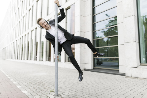Happy young businessman wearing headphones jumping at lamp post in the city stock photo