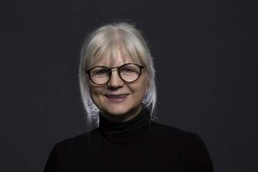 Portrait of smiling senior woman wearing glasses in front of dark background - AWF00095