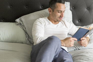 Mittlerer erwachsener Mann, entspannt auf dem Bett, liest ein Buch - ISF12662