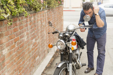 Mittlerer erwachsener Mann, der seine Haare im Seitenspiegel eines Motorrads kontrolliert - ISF12665