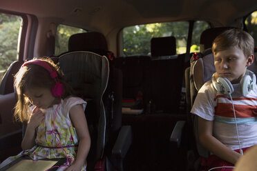 Junge beobachtet jüngere Schwester, die auf dem Rücksitz eines Autos ein digitales Tablet benutzt - ISF12687