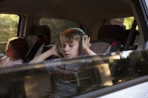 Junge mit jüngerer Schwester hört Kopfhörer auf dem Rücksitz eines Autos, lizenzfreies Stockfoto