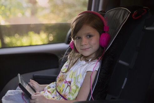 Porträt eines Mädchens mit rosa Kopfhörern und digitalem Tablet im Auto - ISF12691