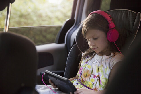 Mädchen mit rosa Kopfhörern, das im Auto ein digitales Tablet benutzt - ISF12692