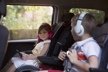 Junge und jüngere Schwester tragen Kopfhörer und benutzen ein digitales Tablet auf dem Rücksitz eines Autos - ISF12693