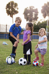 Boy and younger sisters with footballs on practice pitch - ISF12697