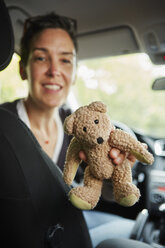 Frau sitzt im Auto und reicht Teddybär durch die Sitze - ISF12709