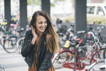 Portrait of happy young woman at bicycle parking station in the city - KNSF03984