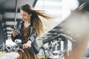 Junge Frau mit Fahrrad und Mobiltelefon in der Stadt - KNSF03989