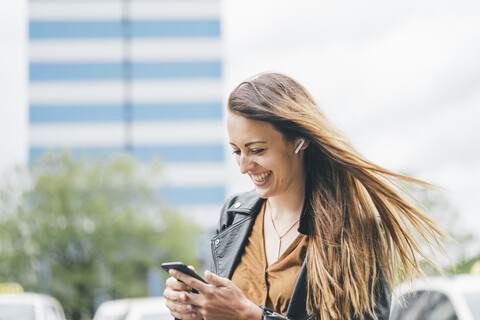 Happy young woman with windswept hair using cell phone in the city stock photo