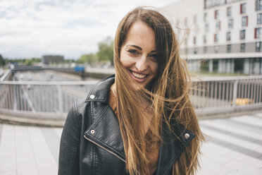 Porträt einer lächelnden jungen Frau mit vom Wind zerzaustem Haar auf einer Autobahnbrücke - KNSF03998