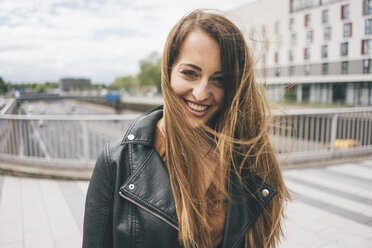 Portrait of smiling young woman with windswept hair on motorway bridge - KNSF03998