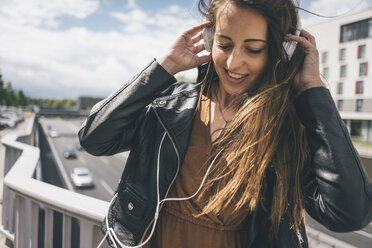 Smiling young woman listening to music on motorway bridge - KNSF04001