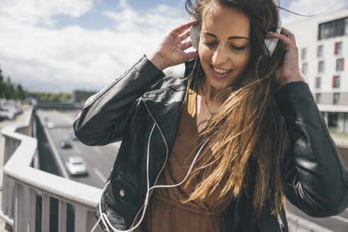 Lächelnde junge Frau beim Musikhören auf einer Autobahnbrücke - KNSF04001