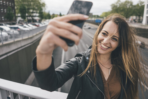 Lächelnde junge Frau macht ein Selfie auf einer Autobahnbrücke, lizenzfreies Stockfoto