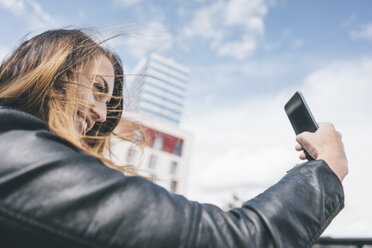 Lächelnde junge Frau macht ein Selfie im Freien - KNSF04003