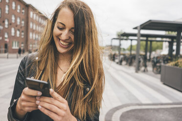 Happy young woman using cell phone in the city - KNSF04007