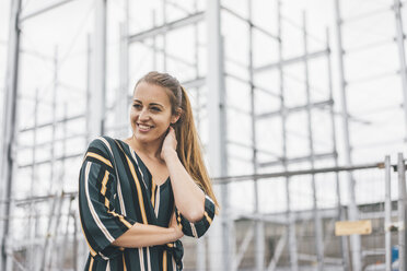 Portrait of smiling young woman at scaffolding - KNSF04011