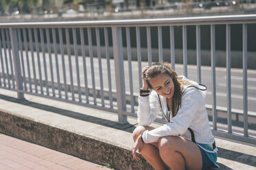 Lächelnde, sportliche junge Frau auf der Autobahn sitzend - KNSF04023