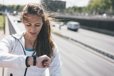 Sportliche junge Frau mit Blick auf die Uhr auf der Autobahn - KNSF04027
