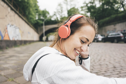 Lächelnde, sportliche junge Frau mit Kopfhörern im Freien - KNSF04036