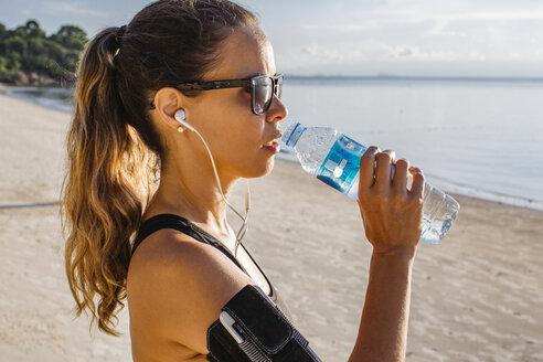 Thailand, Koh Phangan, Sportliche Frau trinkt Wasser am Strand - MOMF00457