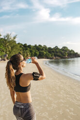 Thailand, Koh Phangan, Sportliche Frau trinkt Wasser am Strand - MOMF00459