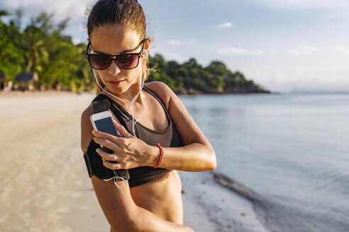 Thailand, Koh Phangan, Sportliche Frau beim Workout am Strand, Smartphone - MOMF00466