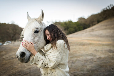 Junge Frau lehnt sich an ein weißes Pferd auf einem Feld und streichelt es - ISF12771