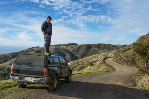 Mann blickt vom Dach eines Pick-up-Trucks nach unten, Big Sur, Kalifornien, USA, lizenzfreies Stockfoto
