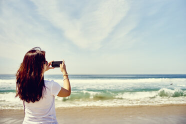 Rückansicht einer Frau am Strand, die den Ozean fotografiert - ISF12827