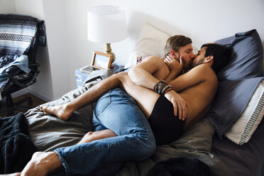 Männliches Paar, teilweise bekleidet, auf dem Bett liegend, küssend - ISF12842