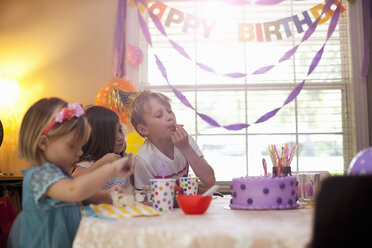 Drei Kinder sitzen am Tisch und essen lila Geburtstagskuchen - ISF12900