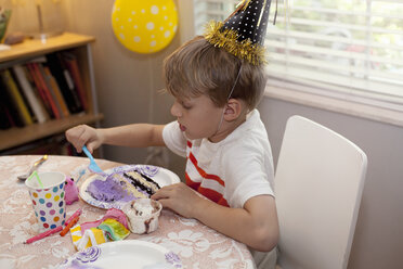 Junge mit Partyhut sitzt am Tisch und isst Geburtstagskuchen - ISF12901