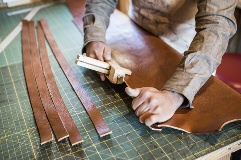 Hände eines Lederhandwerkers, der eine Holzklammer auf einer Werkbank benutzt, lizenzfreies Stockfoto