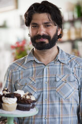 Bäckereibesitzer trägt Tablett mit allergikerfreundlichen Cupcakes - ISF12947