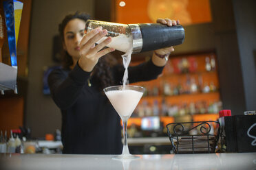Junge Barkeeperin gießt einen Cocktail aus einem Shaker in einer Cocktailbar - ISF12969