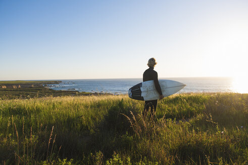 Rear view of young male surfer carrying surfboard looking out to sea - ISF12988