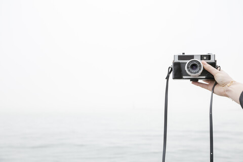Person nimmt Selfie mit Kamera, Meer im Hintergrund, lizenzfreies Stockfoto