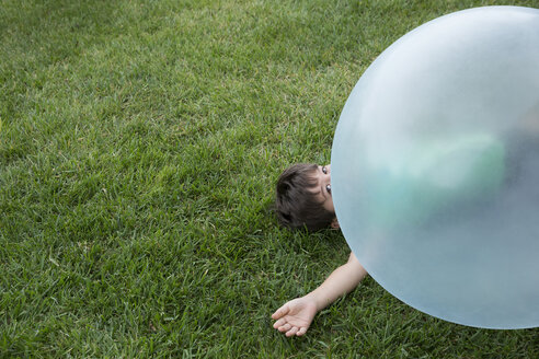 Young boy lying under large inflatable ball - ISF13073