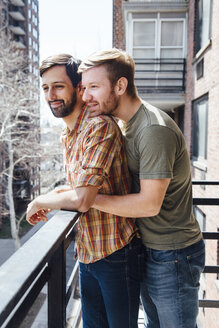 Männliches Paar, das auf einem Balkon steht und die Aussicht betrachtet und sich umarmt - ISF13092