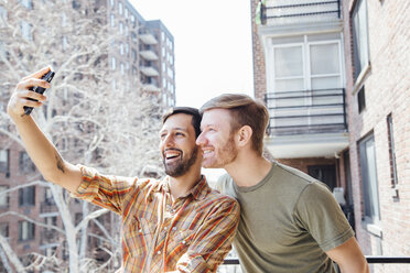 Male couple standing on balcony, taking self portrait, using smartphone - ISF13095