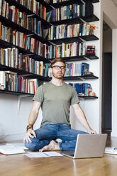 Mid adult man sitting in front of laptop in yoga position - ISF13102