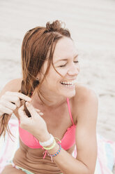 Mid adult woman on beach, plaiting hair - ISF13120