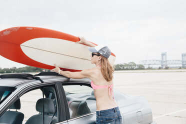 Mittlere erwachsene Frau am Strand, die ein Surfbrett vom Autodach nimmt - ISF13121
